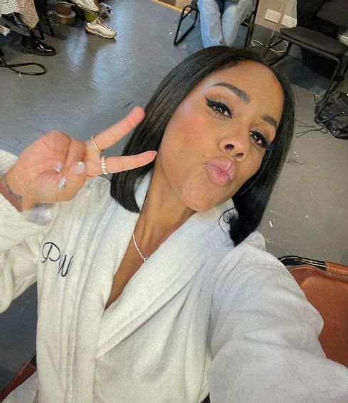 Alex Scott posing in a bath robe whilst giving the peace sign to the camera