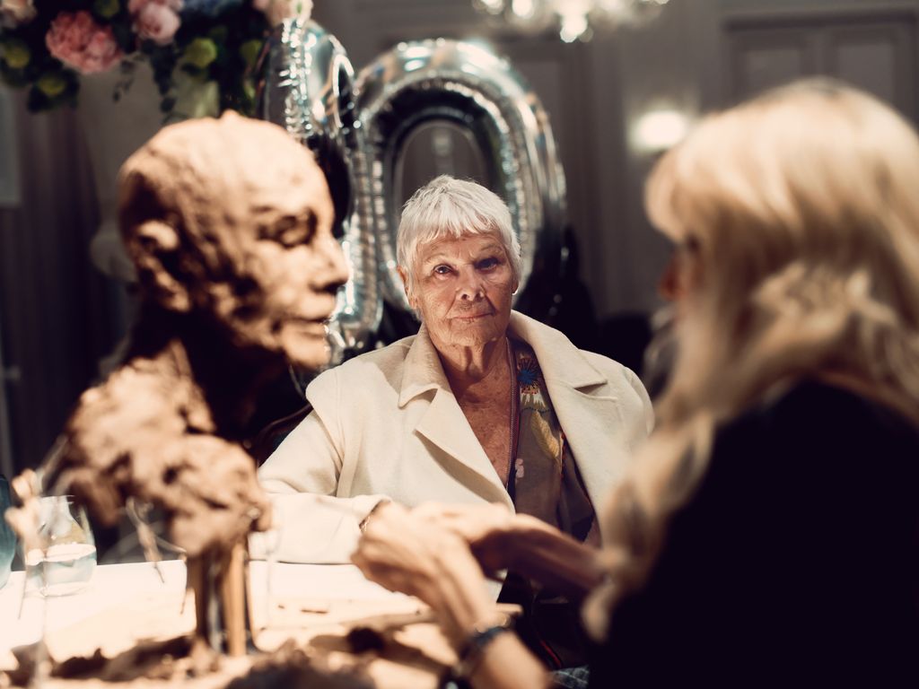 Judi Dench sitting while having a sculpture done of herself