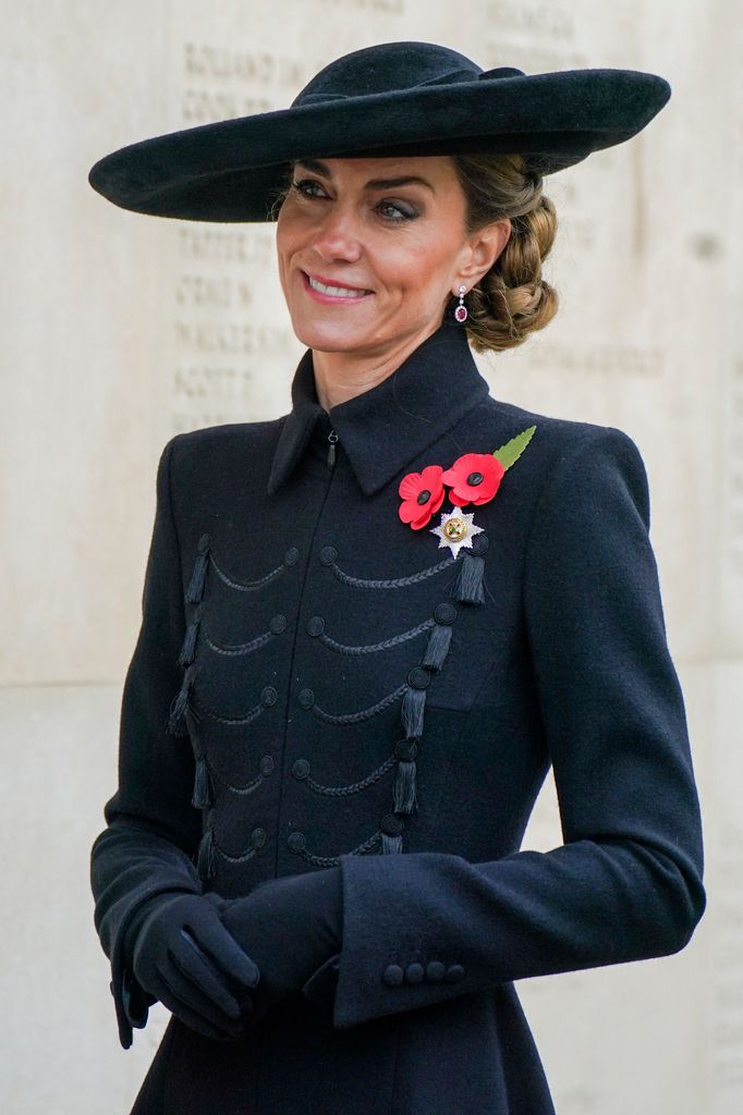 Smiling Kate Middleton wearing black coat, hat and poppies