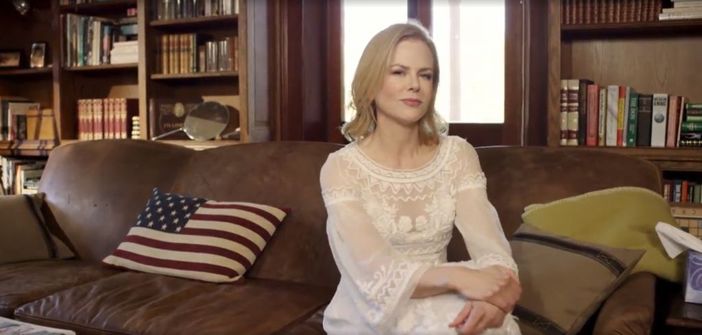 Nicole Kidman in a white dress sitting on a brown leather sofa