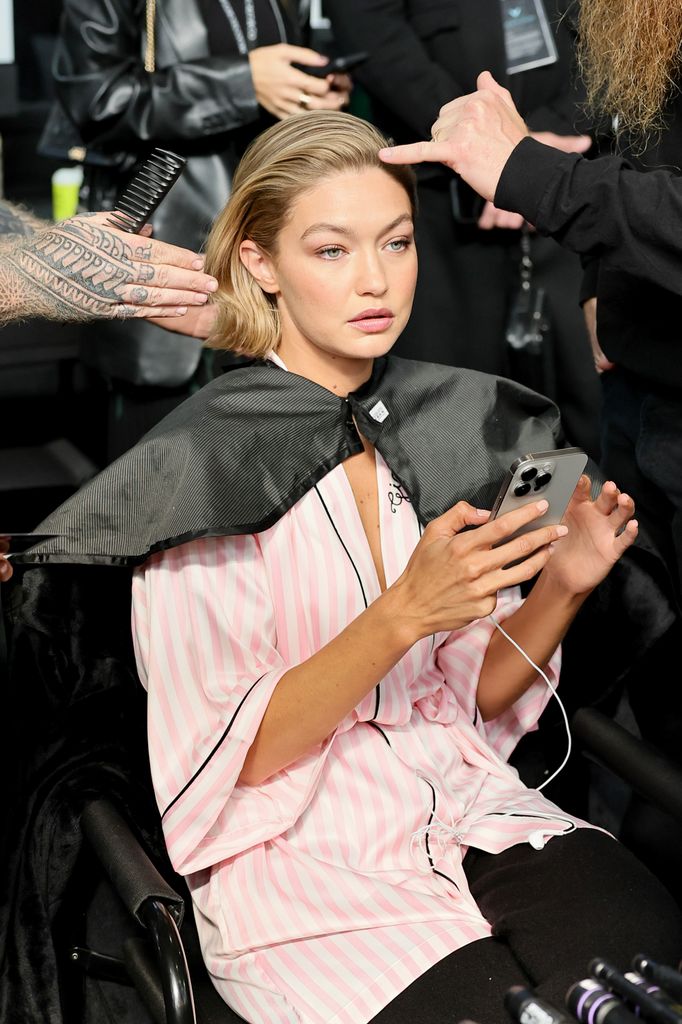 Gigi Hadid was calm and focused as stylists perfected her look. In a pink striped robe and phone in hand, she stayed composed before hitting the runway, capturing that perfect balance of professionalism and serenity behind the scenes.