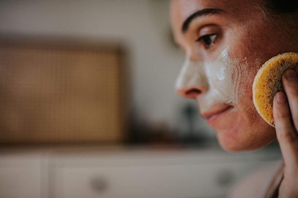 woman cleansing skin with sponge to avoid acne and milia