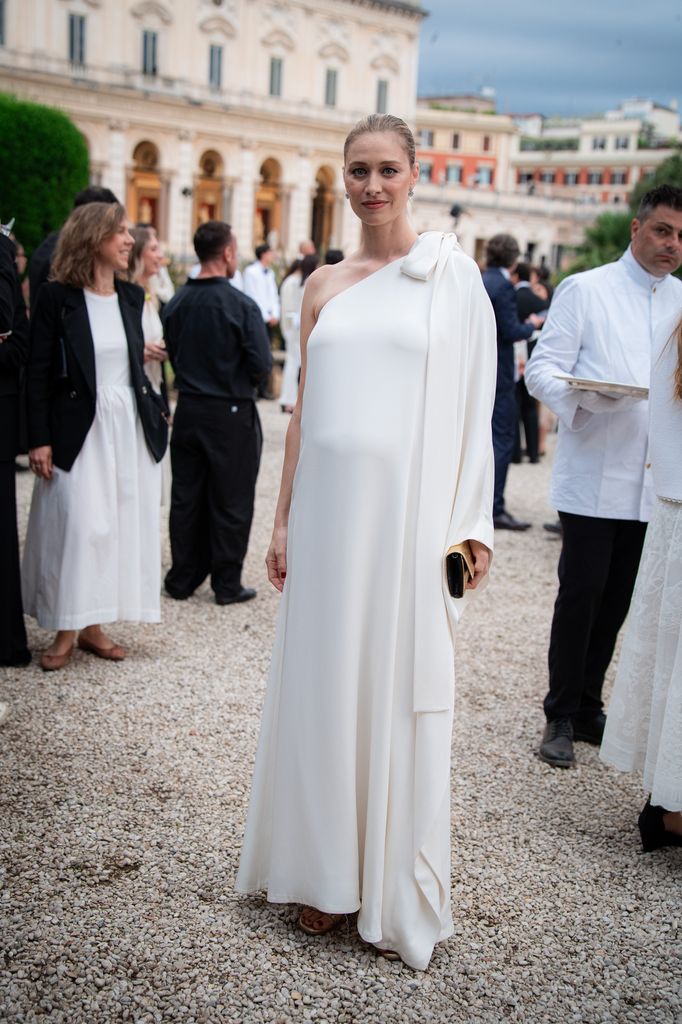 Beatrice Borromeo wears a flowing one-shoulder ivory gown with a knot detail at an elegant garden event in Rome.