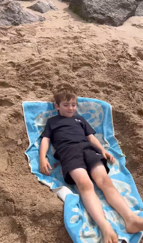 A young boy laid out on a towel on a sandy beach