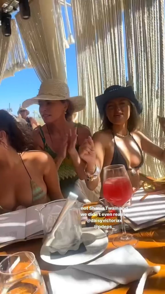 Shania Twain dances between two girls sat down at a table 