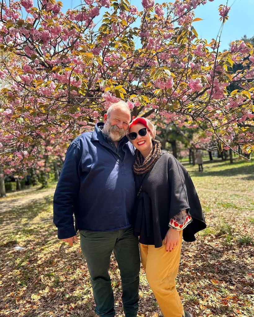 Dick and Angel Strawbridge stand side by side under a blossom tree for a photo