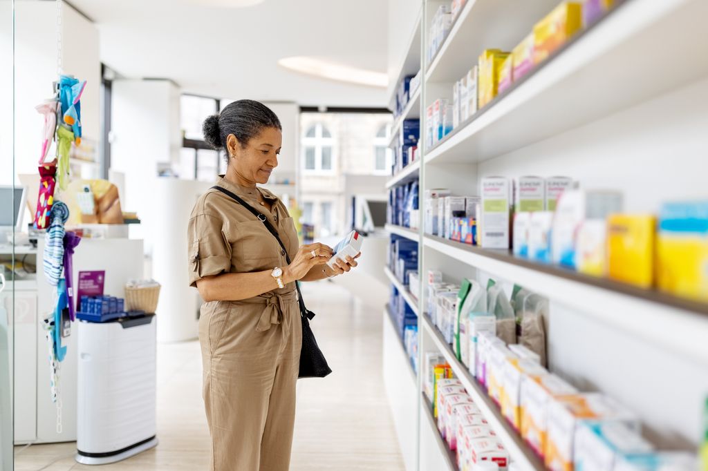 Female customer picking and looking at the medicine box from the shelf. Senior woman buying medicine at drugstore.