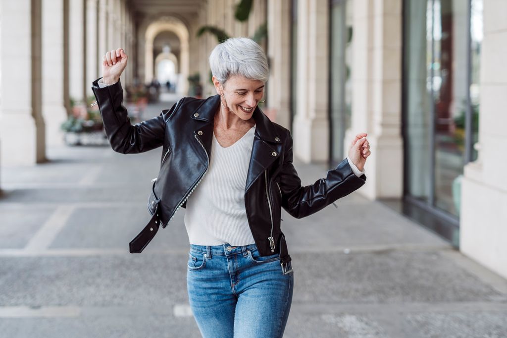 Cheerful and happy mature woman dancing in the middle of the street. Happiness concept.