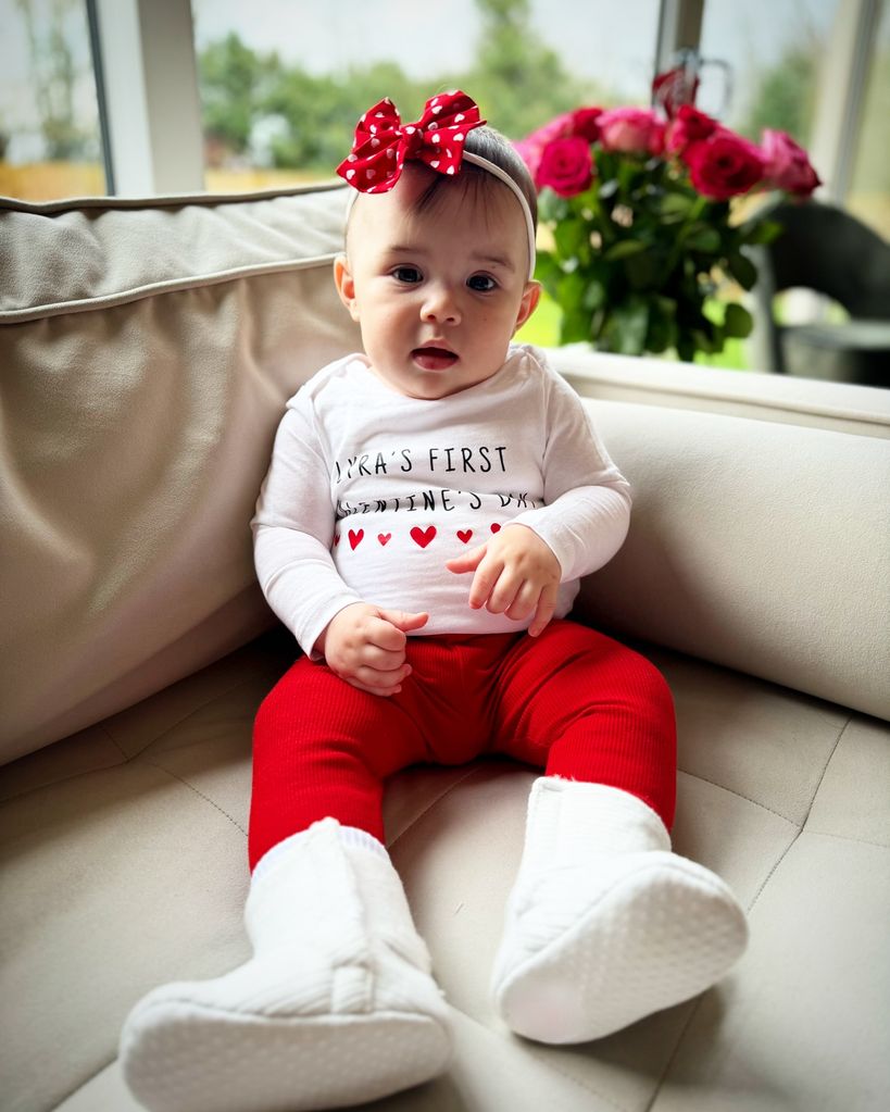 A photo of Lyra Rose wearing red leggings and a white baby grow