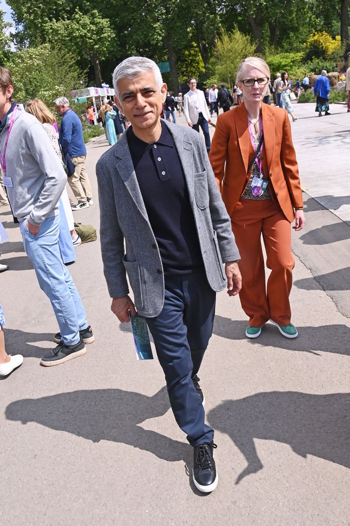 Sadiq Khan at Chelsea Flower Show 2025 in a grey blazer, navy polo shirt and navy trousers with black sneakers, walking through the RHS grounds with fellow guests.