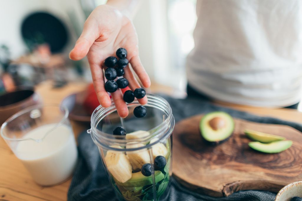 Close-up shot of a female hand putting raw ingredients into a blender to make fresh fruits smoothie.