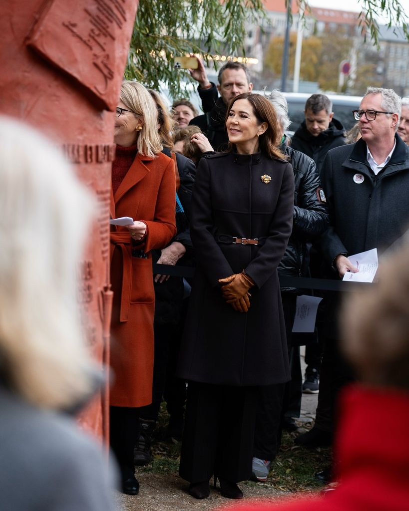 queen mary in navy coat smiling in group of people at statue