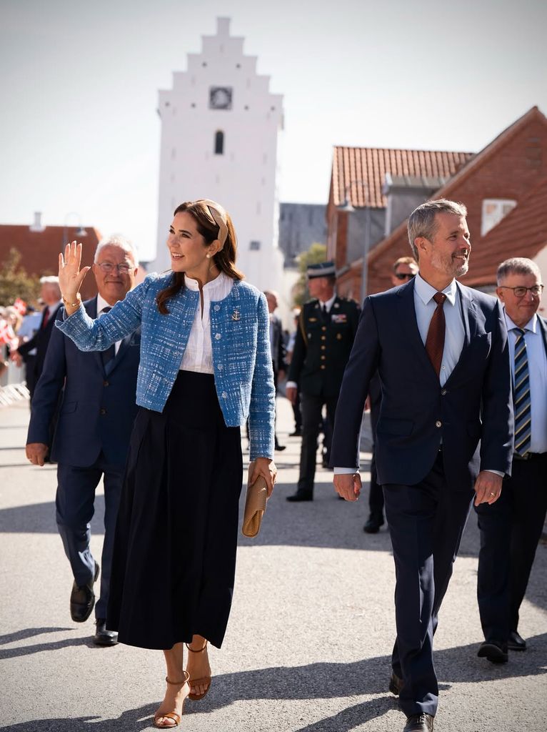 Queen Mary and King Frederik waving as they walk around a small town 