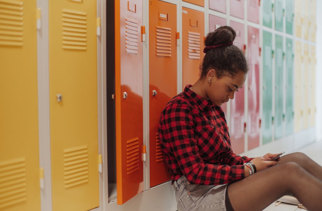 teenage girl sitting in front of lockers on phone