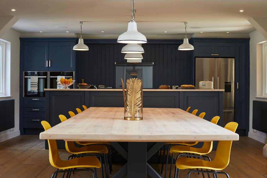 Large navy blue kitchen with yellow chairs and a gold lead vase