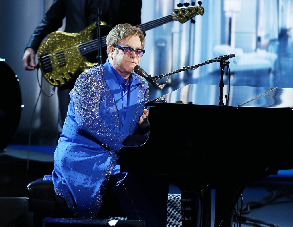 Elton John in a blue suit sitting at a piano