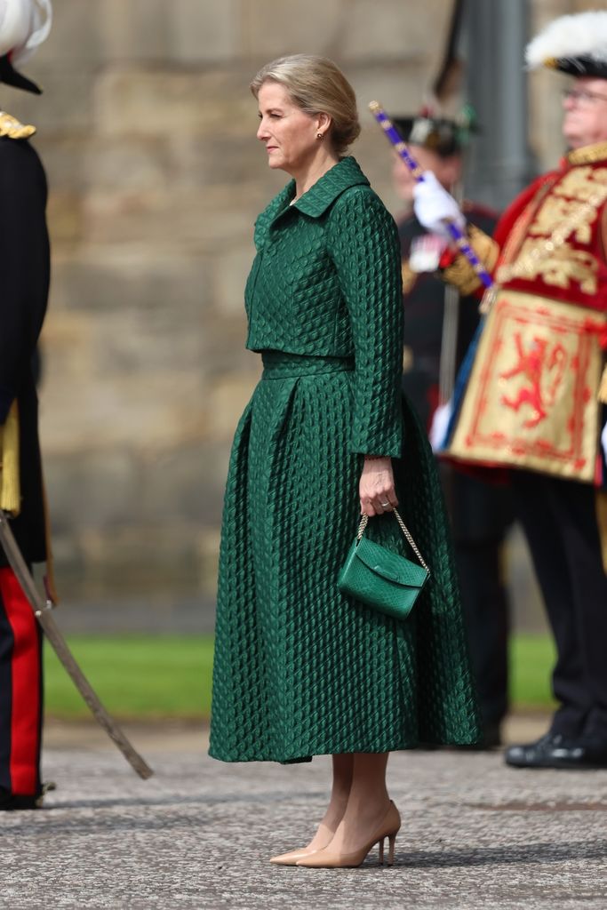 Sophie em posição de sentido com saia e jaqueta verdes