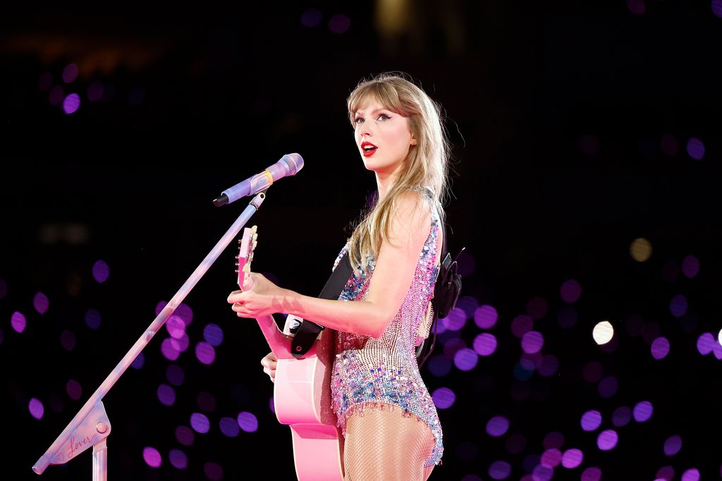 Taylor Swift playing guitar on stage in a glittering bodysuit