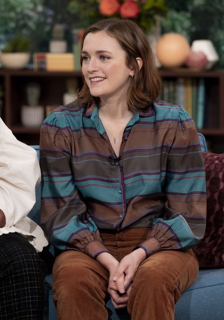 Charlotte Ritchie in a blue and black stripped shirt sitting on a sofa