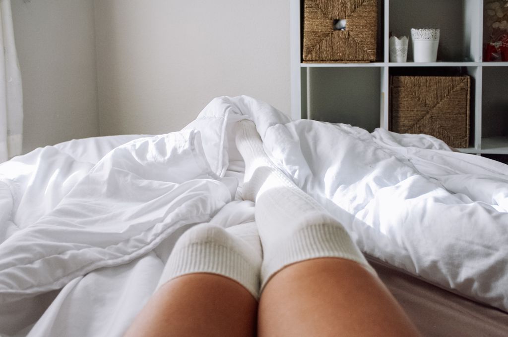 Unrecognizable woman in bed with legs with long socks in winter and autumn