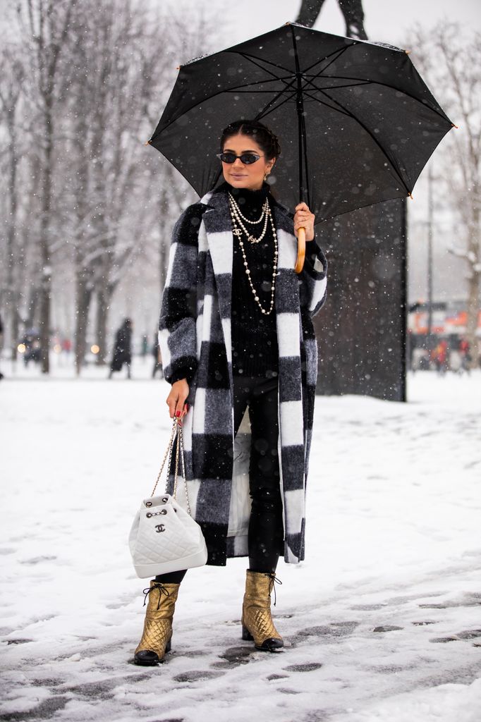 Thassia Naves wears checkered coat with black layers underneath, accented by gold boots and a chic white purse. With layered pearls, this look combines elegance with edge, making it ideal for a day out in the snow