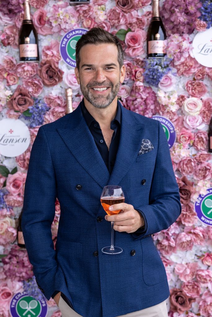 Gethin Jones in a blue suit against a pink floral wall