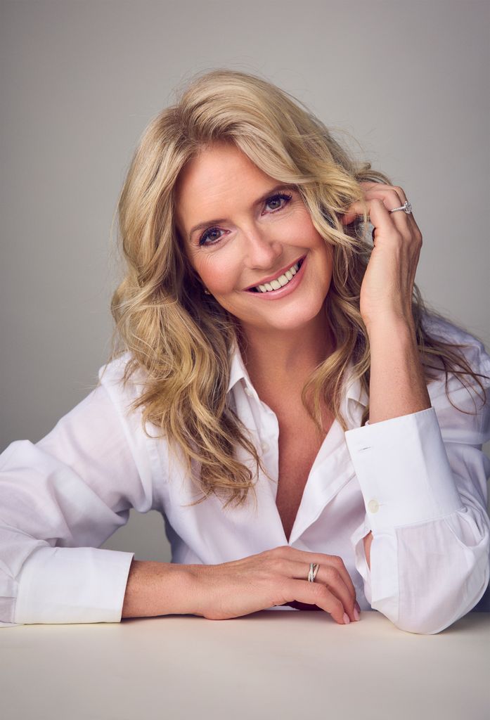 Penny Lancaster smiling with her head resting on her hand in a white shirt