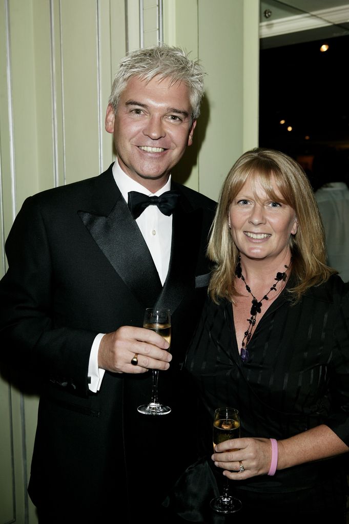 Phillip Schofield holding a drink in a suit and bow tie with his wife Stephanie in a black dress