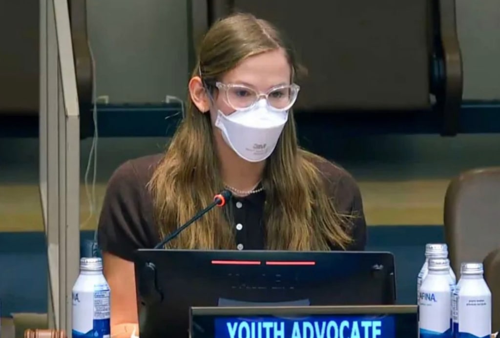 Violet in brown top wearing white mask and glasses at United Nations 