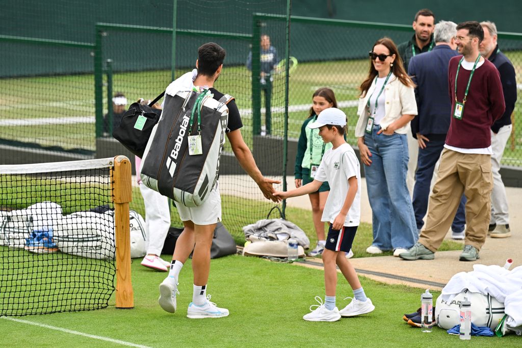Novak Djokovic and son Stefan on a tennis court with a group of people