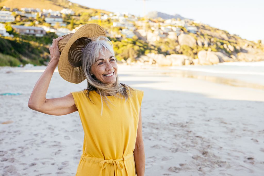 woman with greying hair taking hat off on beach