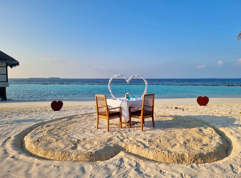 A table and chairs are set up for a couple to dine on the beach at Nova Maldives