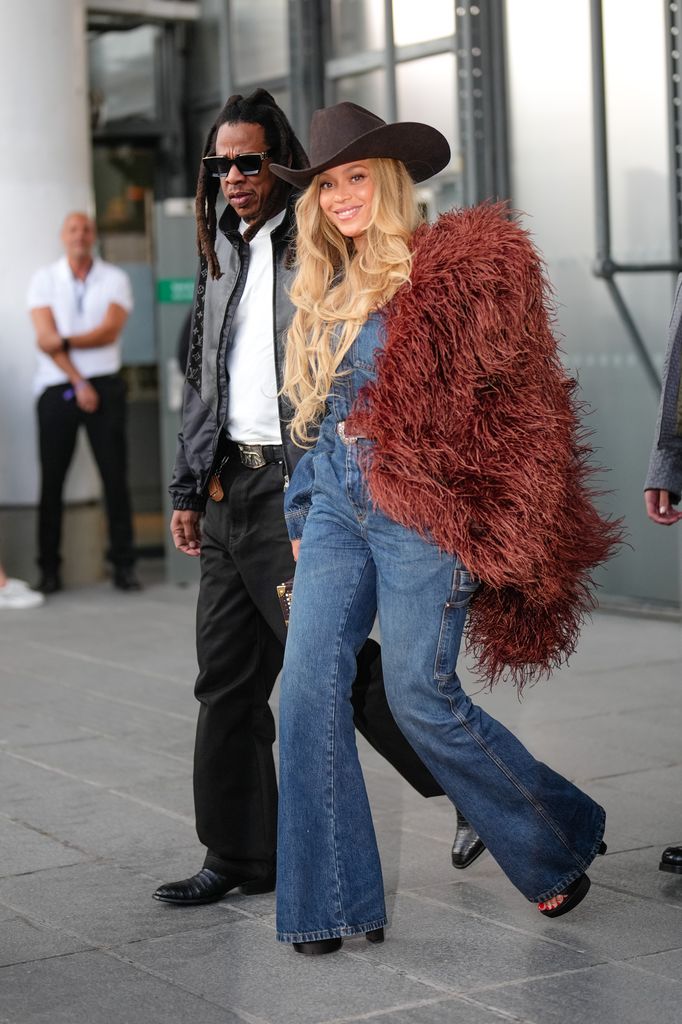 Jay-Z wears a black leather jacket with Louis Vuitton monogram logo print, a white t-shirt, a belt, black wide-leg pants, black leather pointed shoes ; Beyonce wears a cowboy hat, a burgundy faux fur fluff coat on one shoulder, a blue denim jacket, blue flared denim pants / jeans, during the Louis Vuitton Menswear Spring/Summer 2026 show as part of Paris Fashion Week on June 24, 2025 in Paris, France. (Photo by Edward Berthelot/Getty Images)