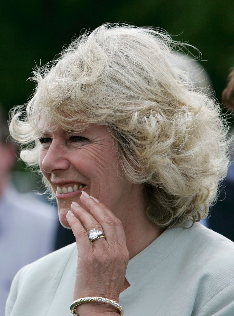 Queen Camilla holding her left hand up to her face and smiling
