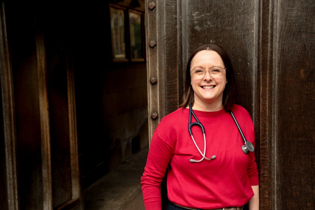 brunette woman in a red top smiling with a stethoscope around her neck
