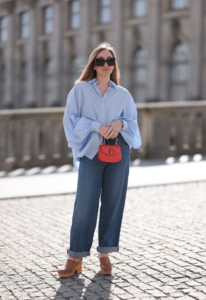  Sonia Lyson seen wearing Saint Laurent black / brown sunglasses, SoSue light blue cotton buttoned oversized shirt, Leviâs dark blue denim straight leg long pants, Gucci bamboo red / orange round leather mini bag and Scholl platform wood 
