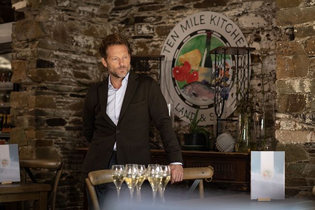 Jamie Bamber as Archie standing in the cafe