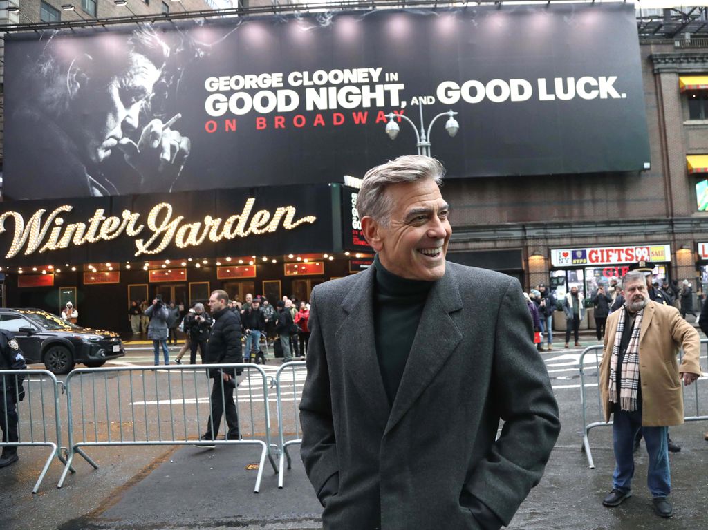 Man in grey suit smiling whilst standing outside theatre