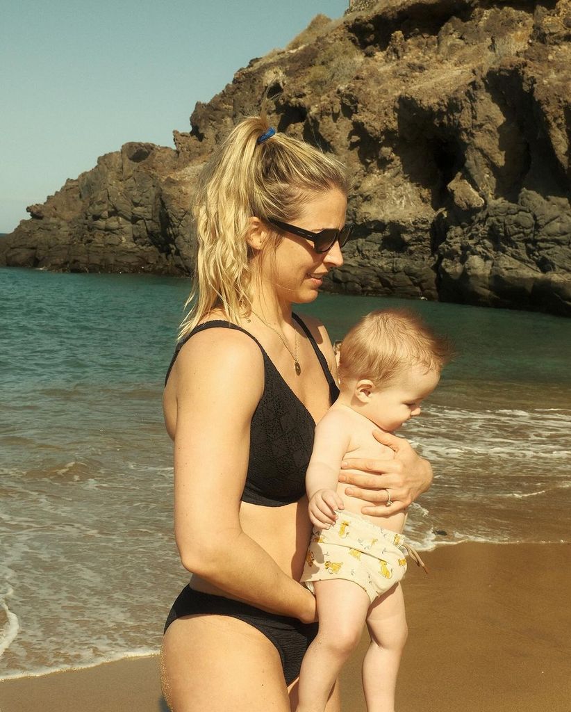 Gemma Atkinson in a black bikini holding baby Thiago on the beach