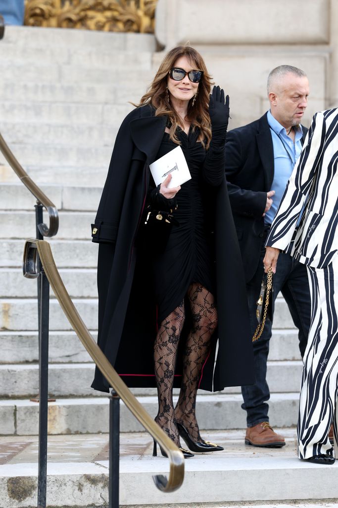 Carla Bruni donned a ruched black dress with lace tights, a cape coat, dramatic sunglasses, and gloves. She embodied Old Hollywood glamour with a contemporary Parisian twist.