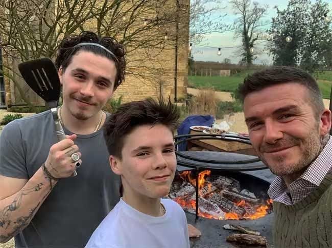 brooklyn cruz and beckham smile at the camera with a barbeque in the background as brooklyn weilds a spatula