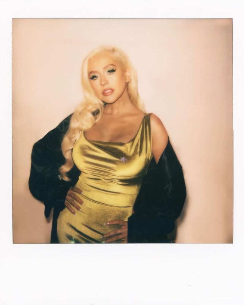 Christina Aguilera posing for polaroid photo in gold dress and black robe