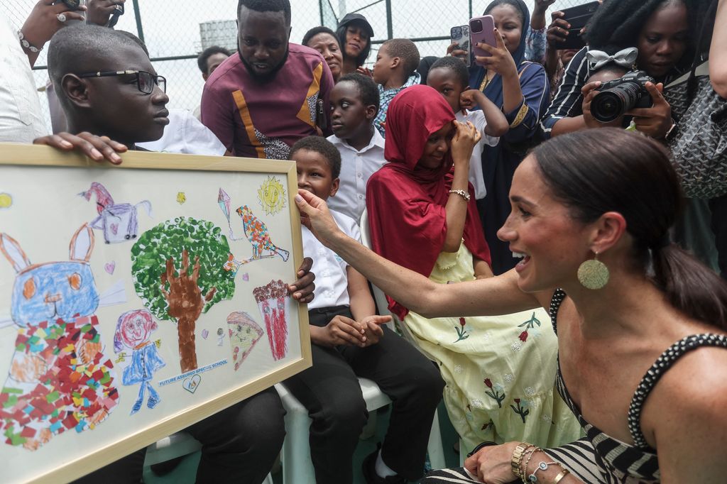Meghan Markle receives an artwork upon her arrival at a sitting volleyball match at Nigeria Unconquered
