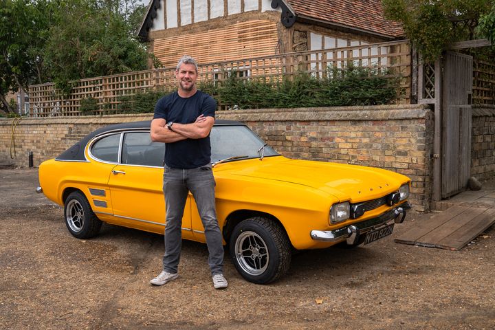 Ant Anstead in black t-shirt and jeans posing in front of yellow car