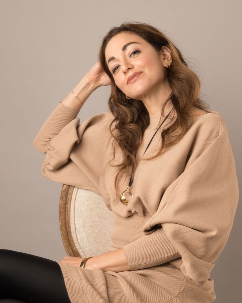 Woman sitting on a chair leaning on her hand in a camel coloured top