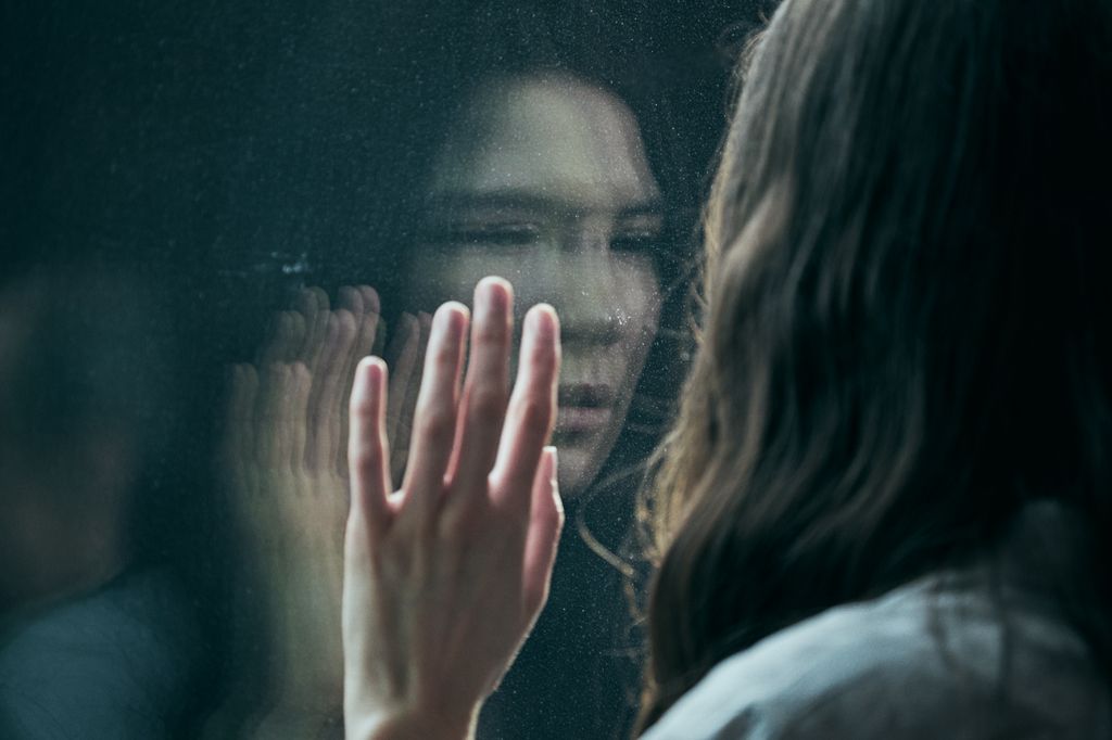 woman with hand on glass looking at reflection