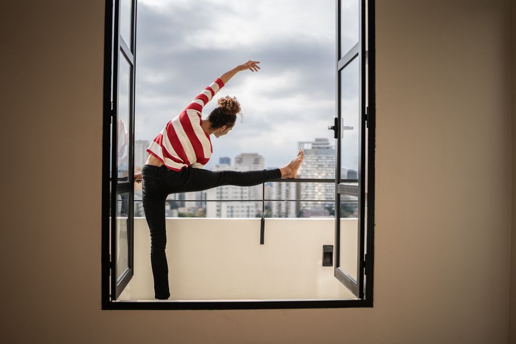 Male ballet dancer stretching in the apartment's balcony