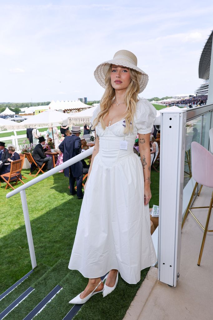 Lottie Moss (wearing Portobello Market hat, House of CB dress, Prada bag, Zara shoes) at Royal Ascot wears a white puff-sleeve corset dress and wide straw sunhat with white heels.