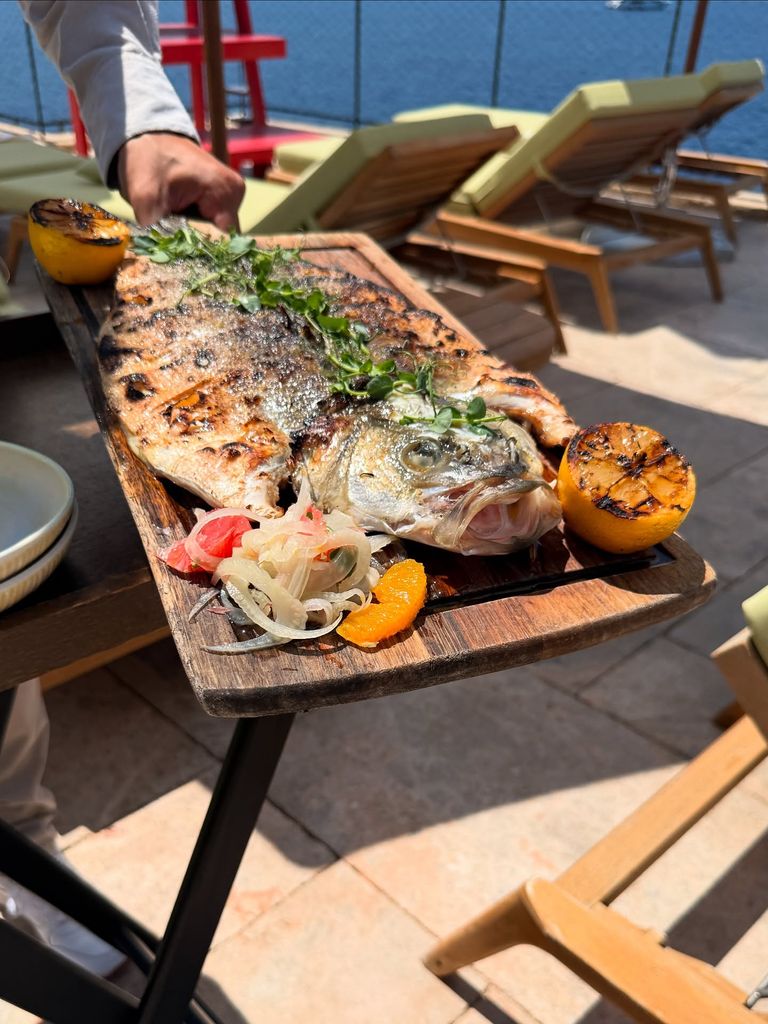 A waiter serves a platter of grilled fish with grilled fruit accompaniments