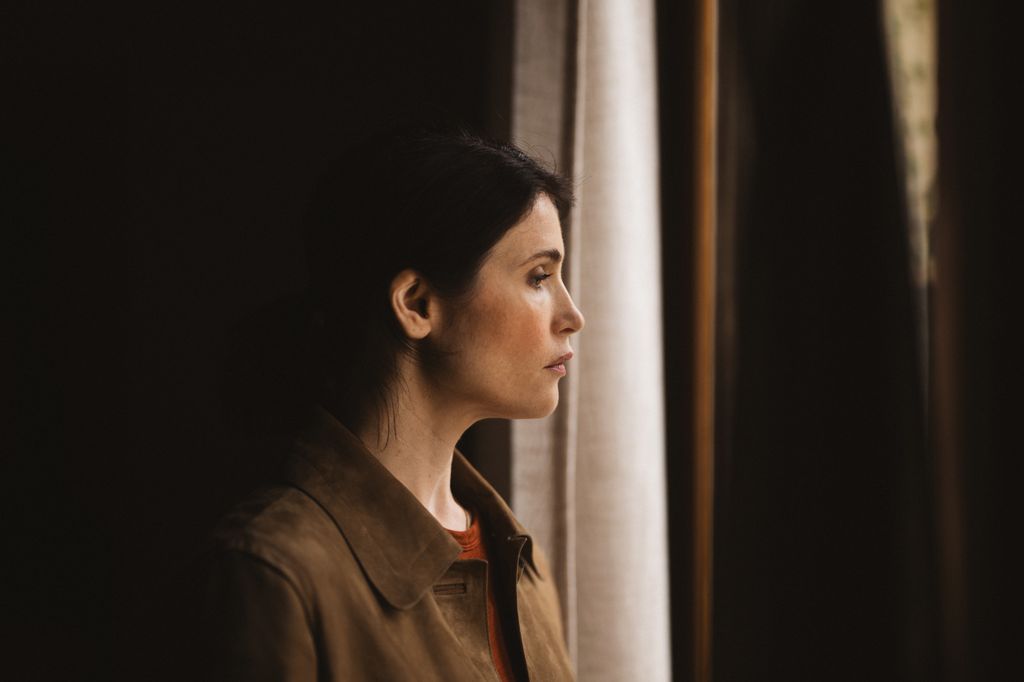 woman looking out window from dimly-lit room